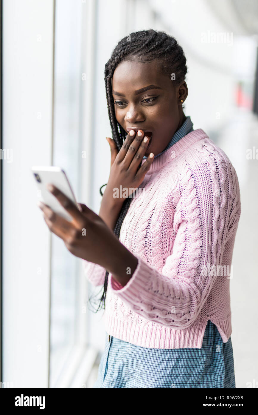 Junge überrascht afro Frau lesen Nachricht vom Telefon vor panoramafenster schockiert Stockfoto