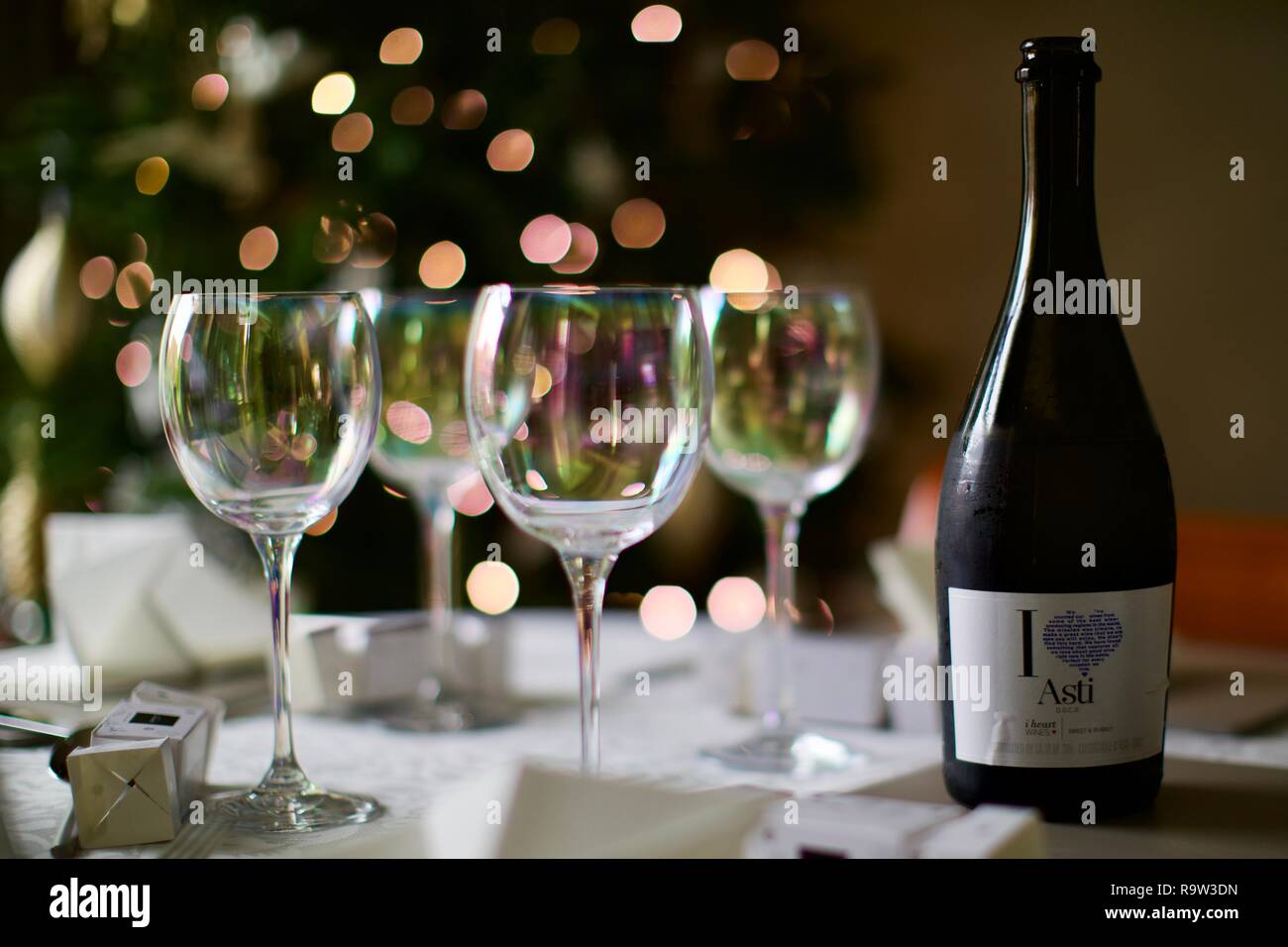 Weingläser und eine Flasche Asti mit Weihnachtsbeleuchtung im Hintergrund Stockfoto