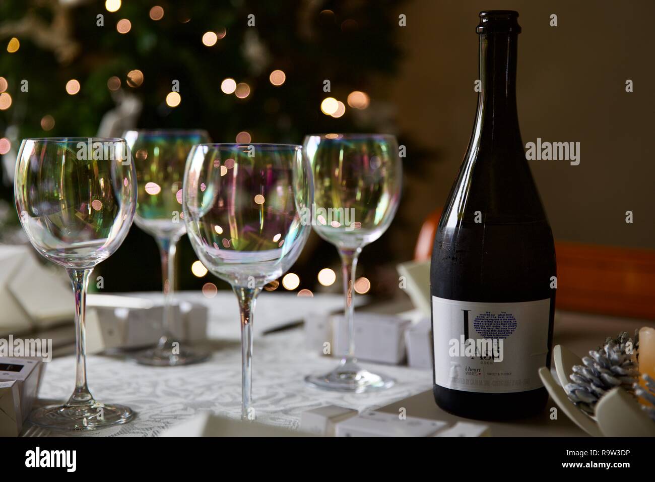 Weingläser und eine Flasche Asti mit Weihnachtsbeleuchtung im Hintergrund Stockfoto
