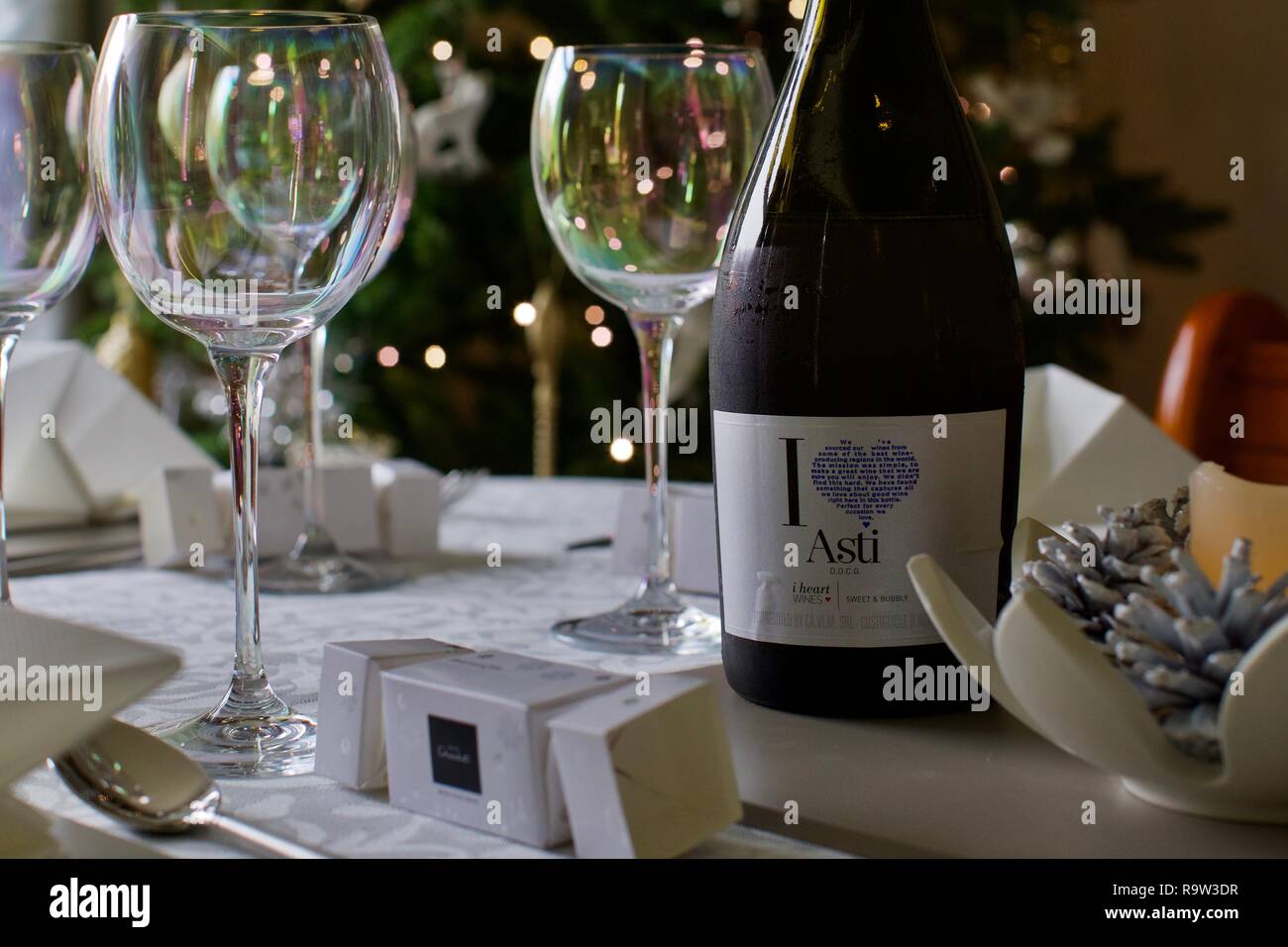 Weingläser und eine Flasche Asti mit Weihnachtsbeleuchtung im Hintergrund Stockfoto