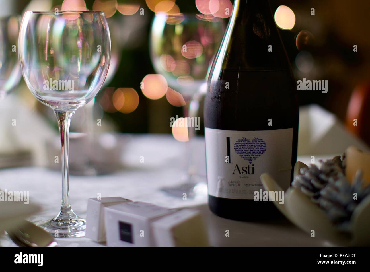 Weingläser und eine Flasche Asti mit Weihnachtsbeleuchtung im Hintergrund Stockfoto
