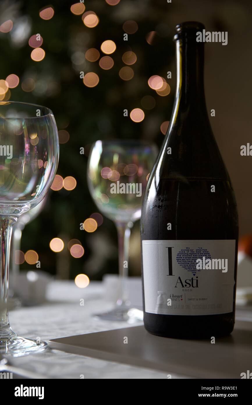 Weingläser und eine Flasche Asti mit Weihnachtsbeleuchtung im Hintergrund Stockfoto