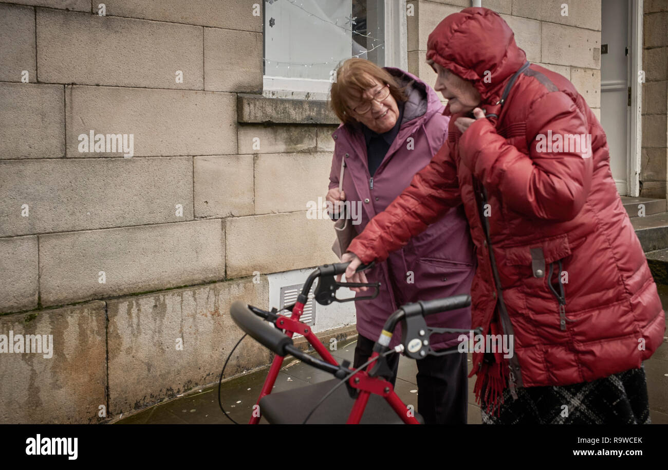 Eine ältere Frau gegen die Kälte und Nässe mit einem Mobilität Walker im Gespräch mit einer anderen Frau, aufgewickelt Stockfoto
