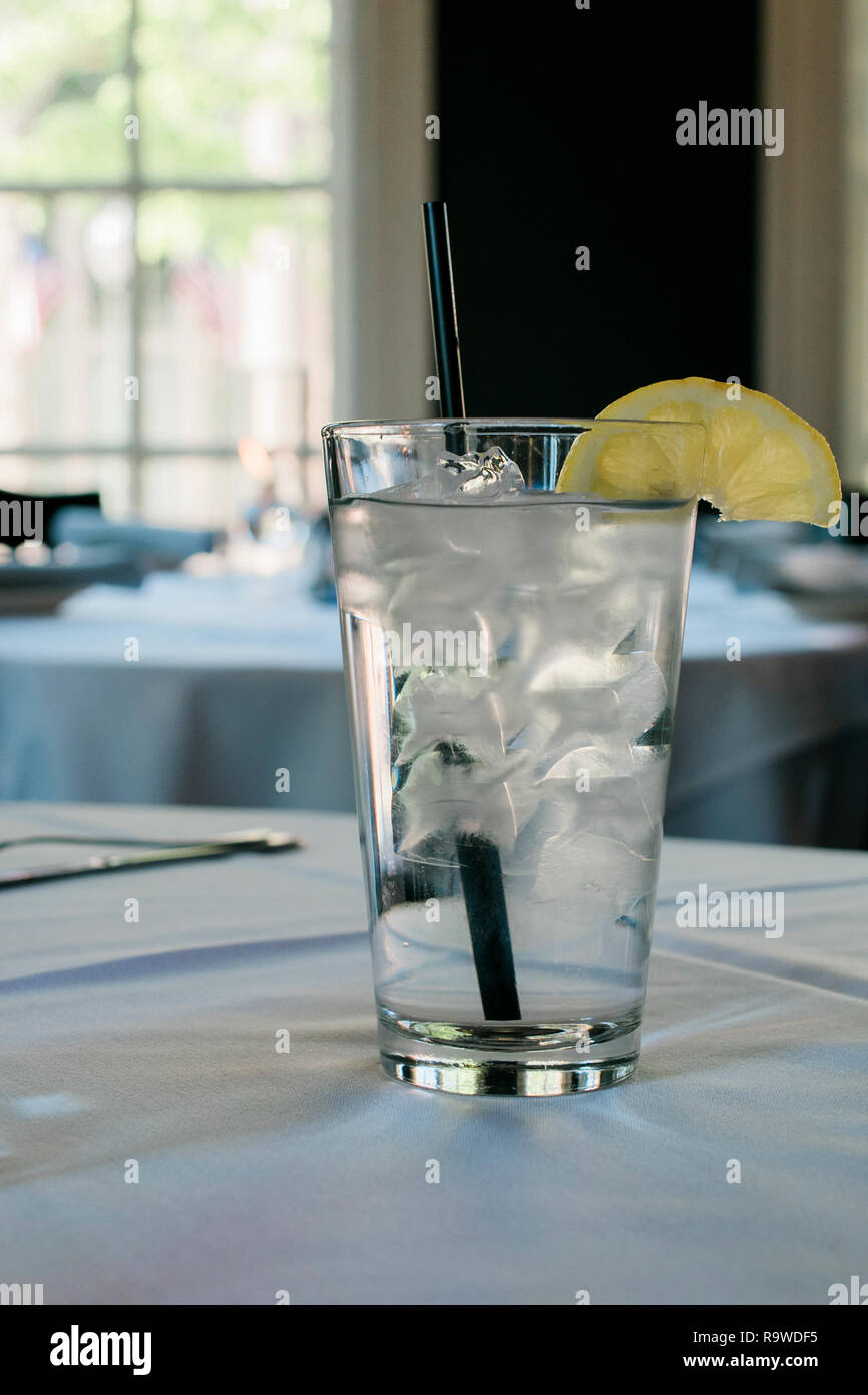 Ein klares Glas mit eiskaltem Wasser mit Zitrone auf einen Tisch. Stockfoto
