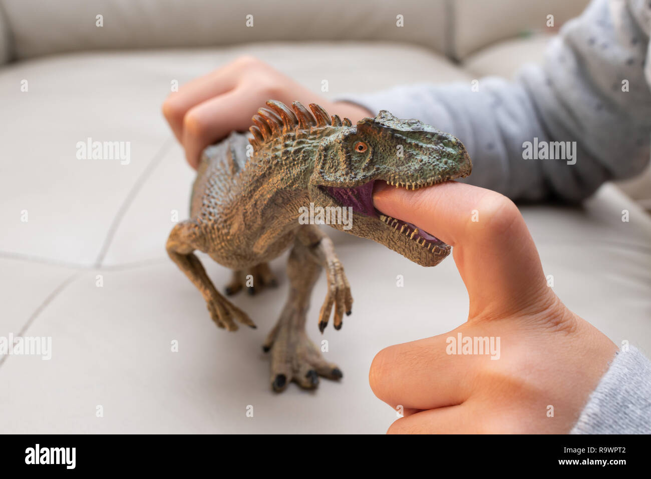 Kid spielen eines allosaurus Spielzeug und seine Finger im Mund Stockfoto