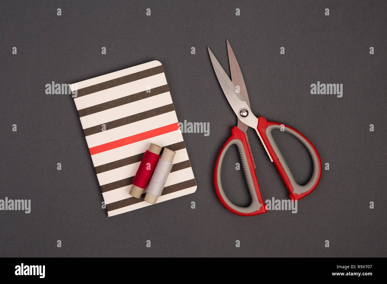 Grauen und roten Faden, Schere und gestreifte Notepad für Hinweise auf grauem Hintergrund Stockfoto