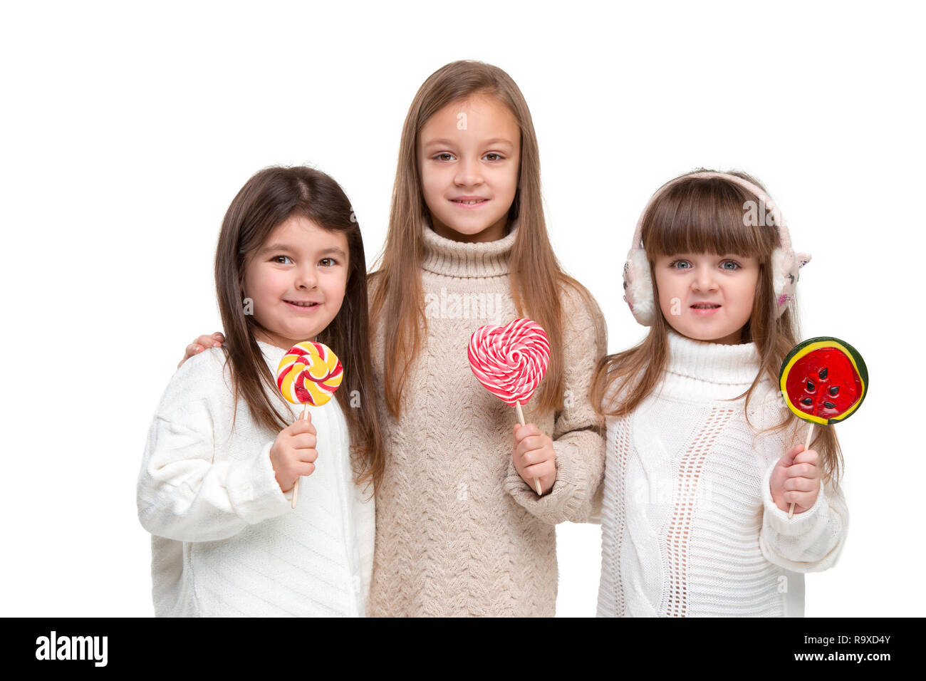 Portrait von niedlichen kleinen Kinder Mädchen im stilvollen gestrickte Pullover mit Süßigkeit an Kamera suchen und lächelnd gegen Weiße studio Wand. Kids Fashion Concept Stockfoto