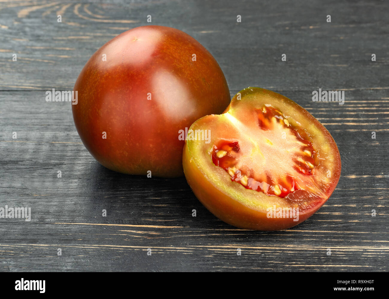 Kumato Tomate mit saftigen Hälfte auf einen dunklen Tisch Stockfoto