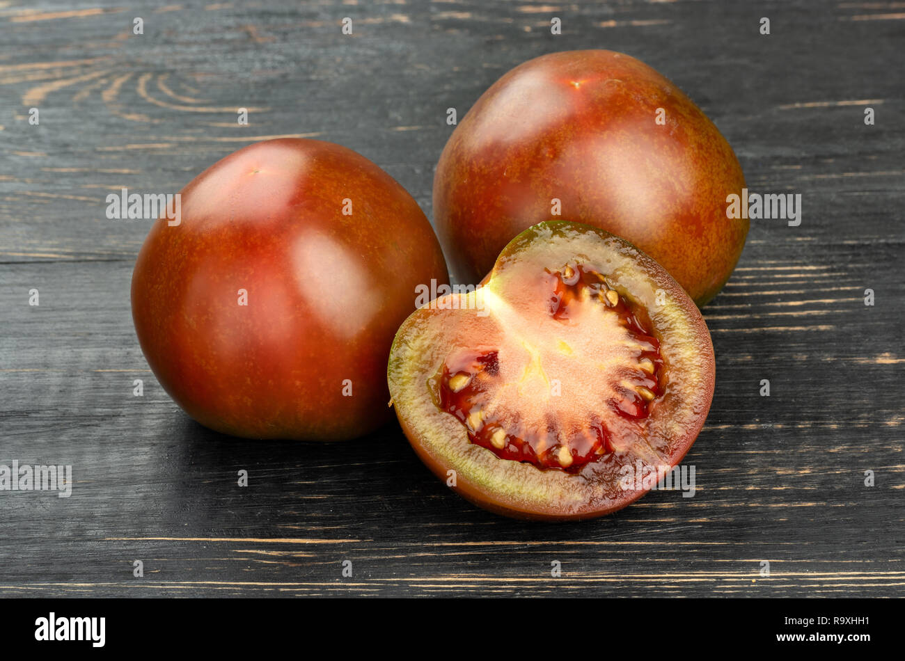 Kumato Tomate mit saftigen Hälfte auf einer hölzernen Hintergrund Stockfoto