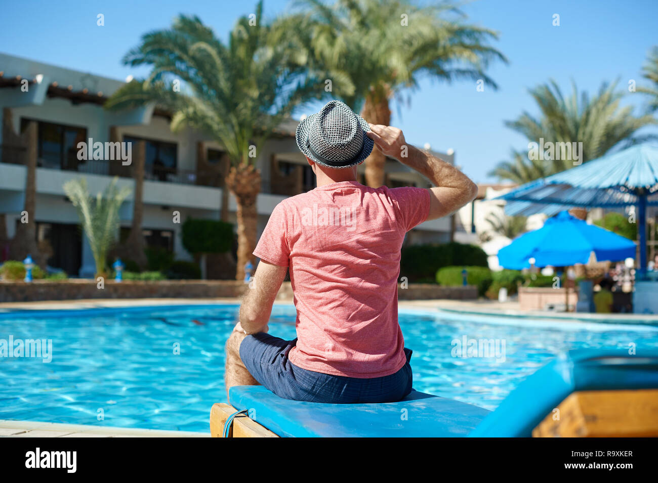 Junger Mann in Hut sitzen auf Sonnenliegen am Schwimmbad Hotel Stockfoto