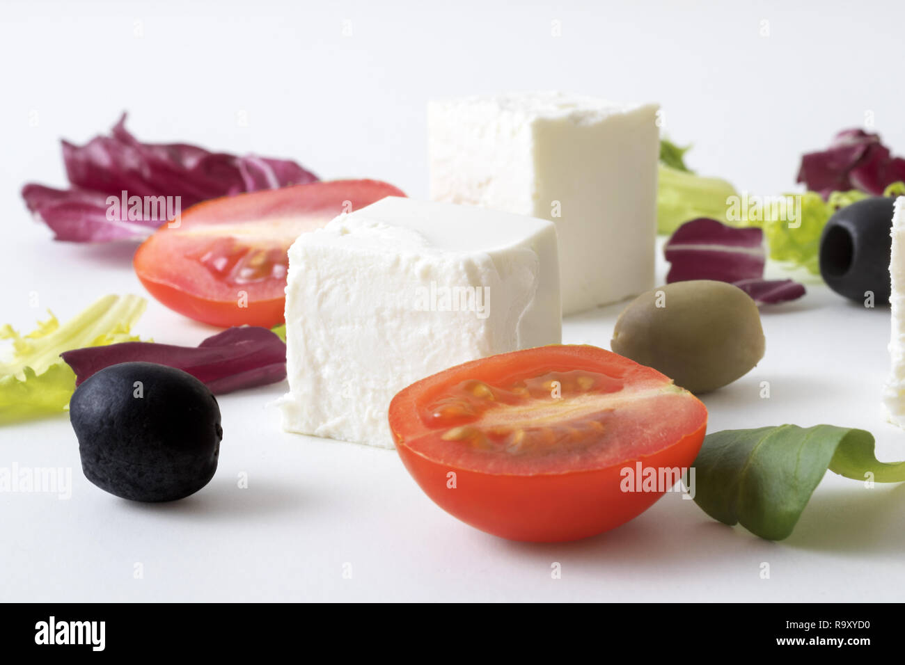 Griechischer Salat, weiß griechischer Käse, grüne und schwarze Oliven, Salatblätter, Hälften der Kirsche Tomate. Hintergrund weiss Variationen von salatblättern und Feta Stockfoto