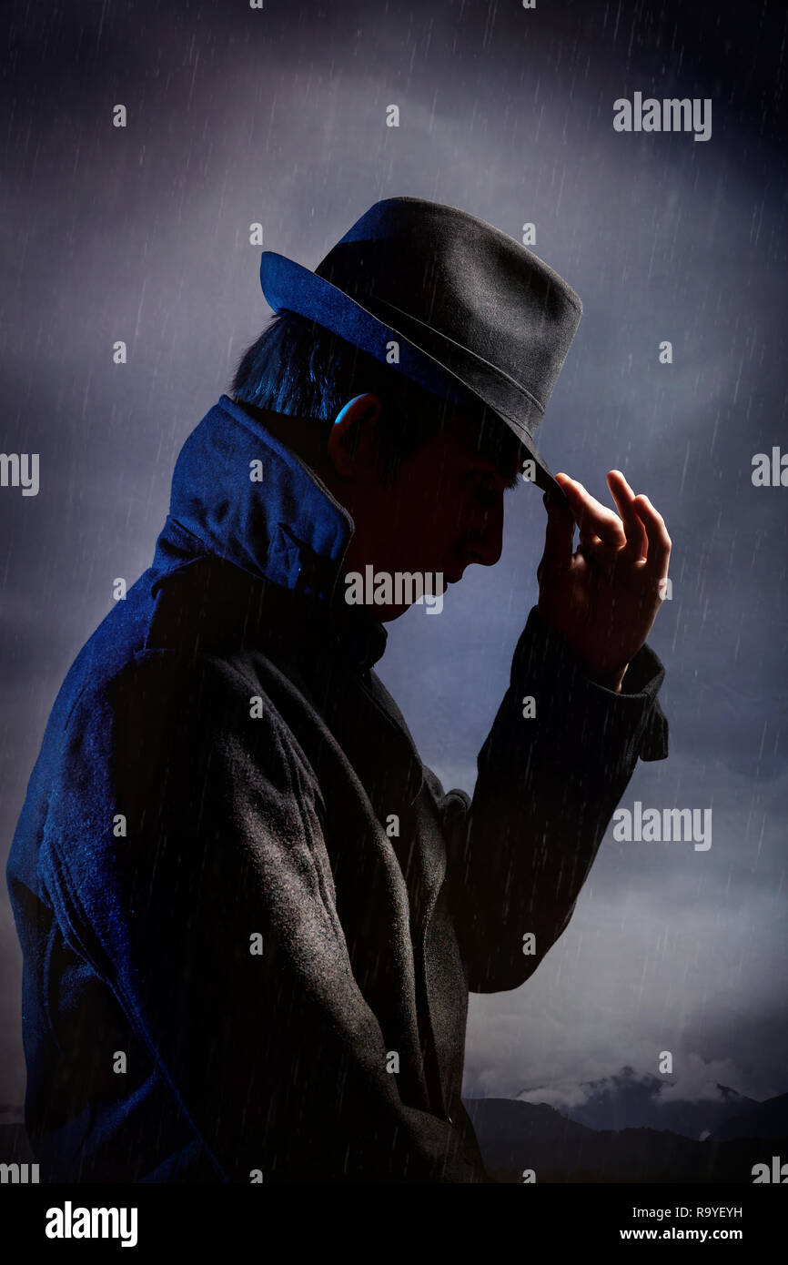 Mann in schwarzen Hut im Regen an der Dunkelheit bedeckten Himmel Stockfoto