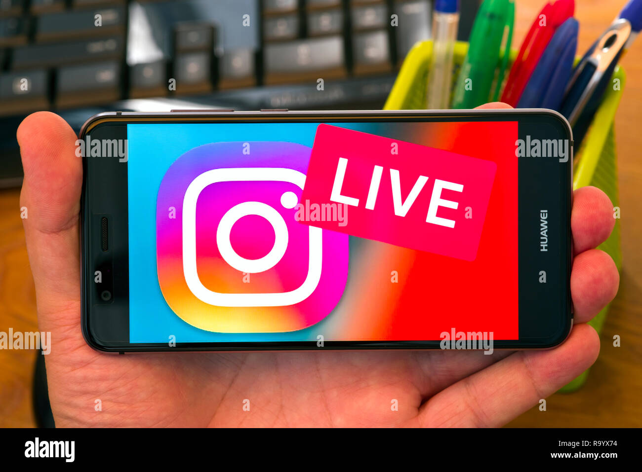 PIATRA Neamt, Rumänien - 30. JULI 2018: Hand hält ein Mobiltelefon mit Instagram Live Logo auf dem Bildschirm angezeigt, Büro Hintergrund. Stockfoto