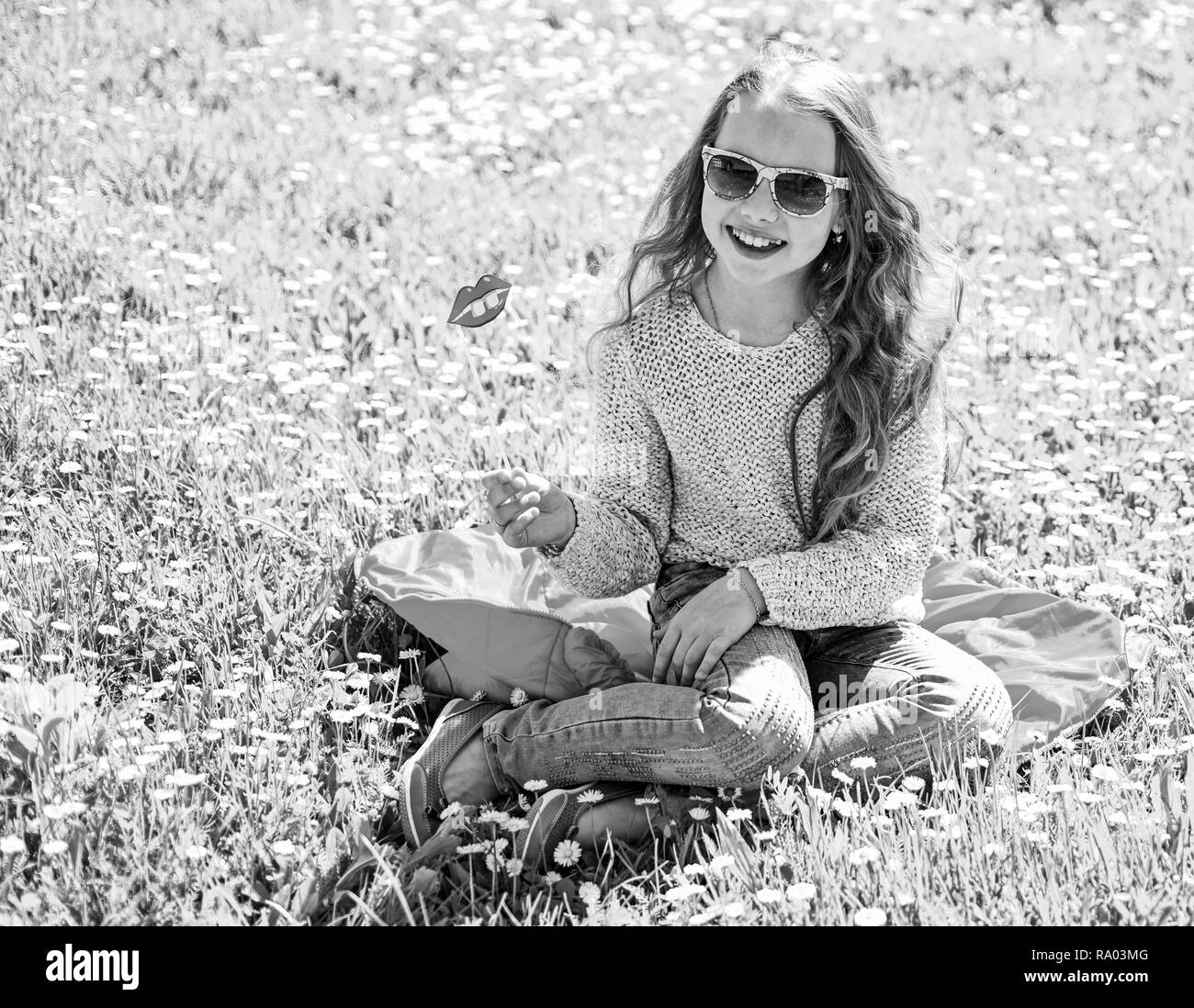 Mädchen sitzt auf Gras an grassplot, grünen Hintergrund. Kind posiert mit Sonnenbrille Pappe ein Lächeln auf den Lippen an der Wiese. Mädchen auf fröhliche Gesicht verbringen Freizeitaktivitäten im Freien. Fashionista Konzept. Stockfoto
