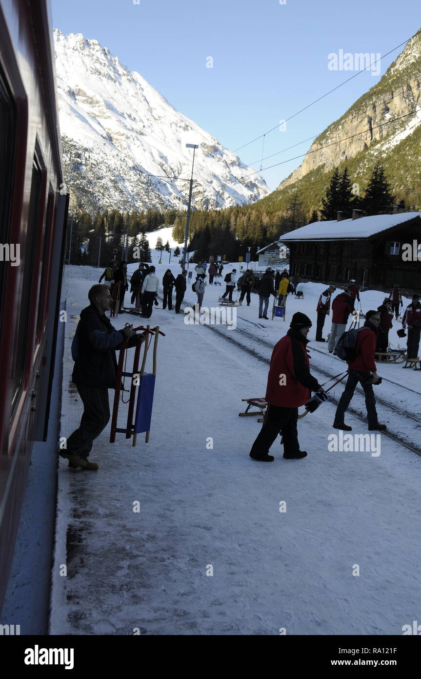 Passagiere, die ihre Schlitten, Aussteigen aus einem Rhatische Bahn Personenzug in Preda Bahnhof in der Schweiz. Die Preda-Bergun Rodelbahn r Stockfoto