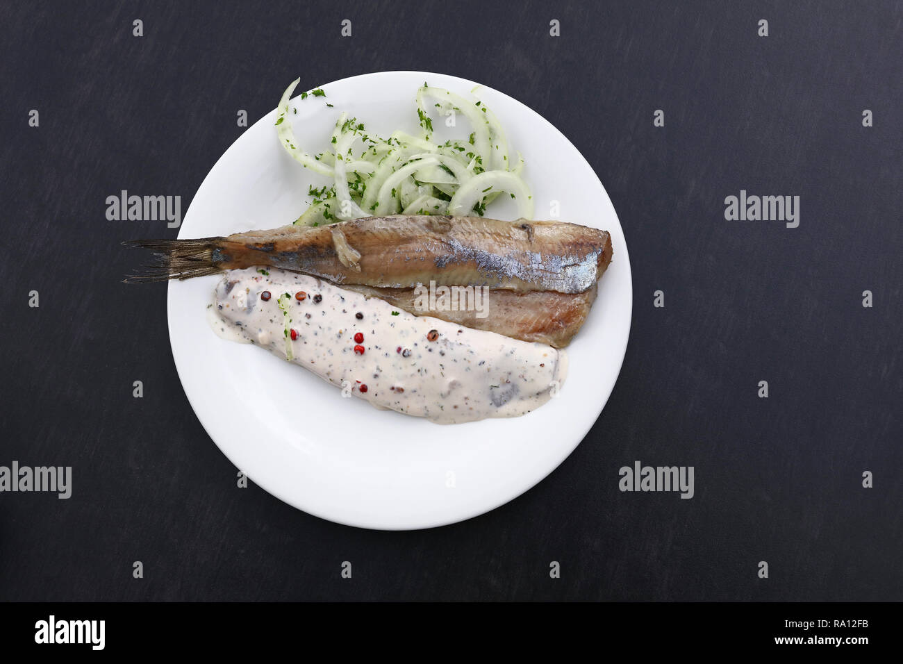 Close up Teil Salzwasser eingelegte Hering Fischfilets mit Zwiebeln und Soße auf weiße Platte über schwarzen Tisch, Erhöhte Ansicht von oben, direkt über Stockfoto