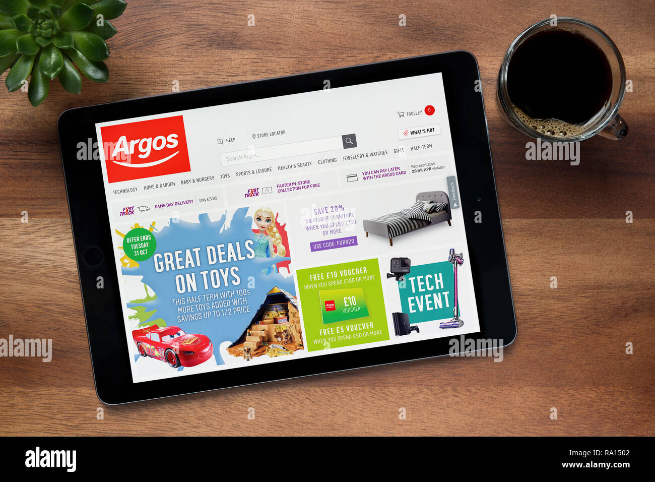 Die Website von Argos ist auf einem iPad Tablet gesehen, auf einer hölzernen Tisch zusammen mit einem Espresso und einem Haus Anlage (nur redaktionelle Nutzung). Stockfoto