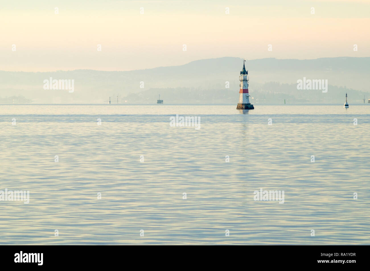 Kleinen weißen Leuchtturm auf rosa Himmel Hintergrund bei Sonnenuntergang isoliert, im Eingang zum Oslo Hafen. Winter- und ruhiges Meer im Inneren Oslofjord Gewässern. Stockfoto