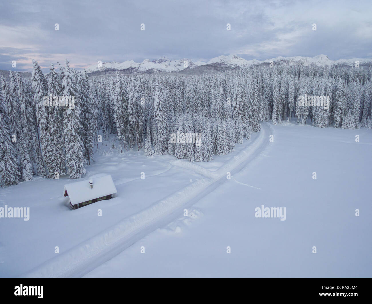 Luftbild von einem Holzhaus neben Wald und Berge im Schnee dahinter abgedeckt im kalten Winter Stockfoto