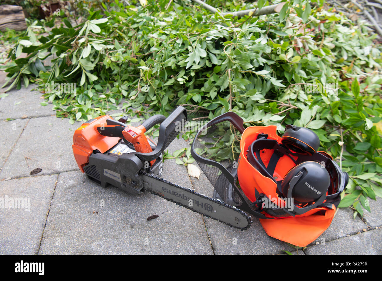 Husqvarna Kettensäge und Helm mit Gehörschutz liegt auf einer Terrasse neben Branchen, die gerade unten geschnitten wurden. Stockfoto