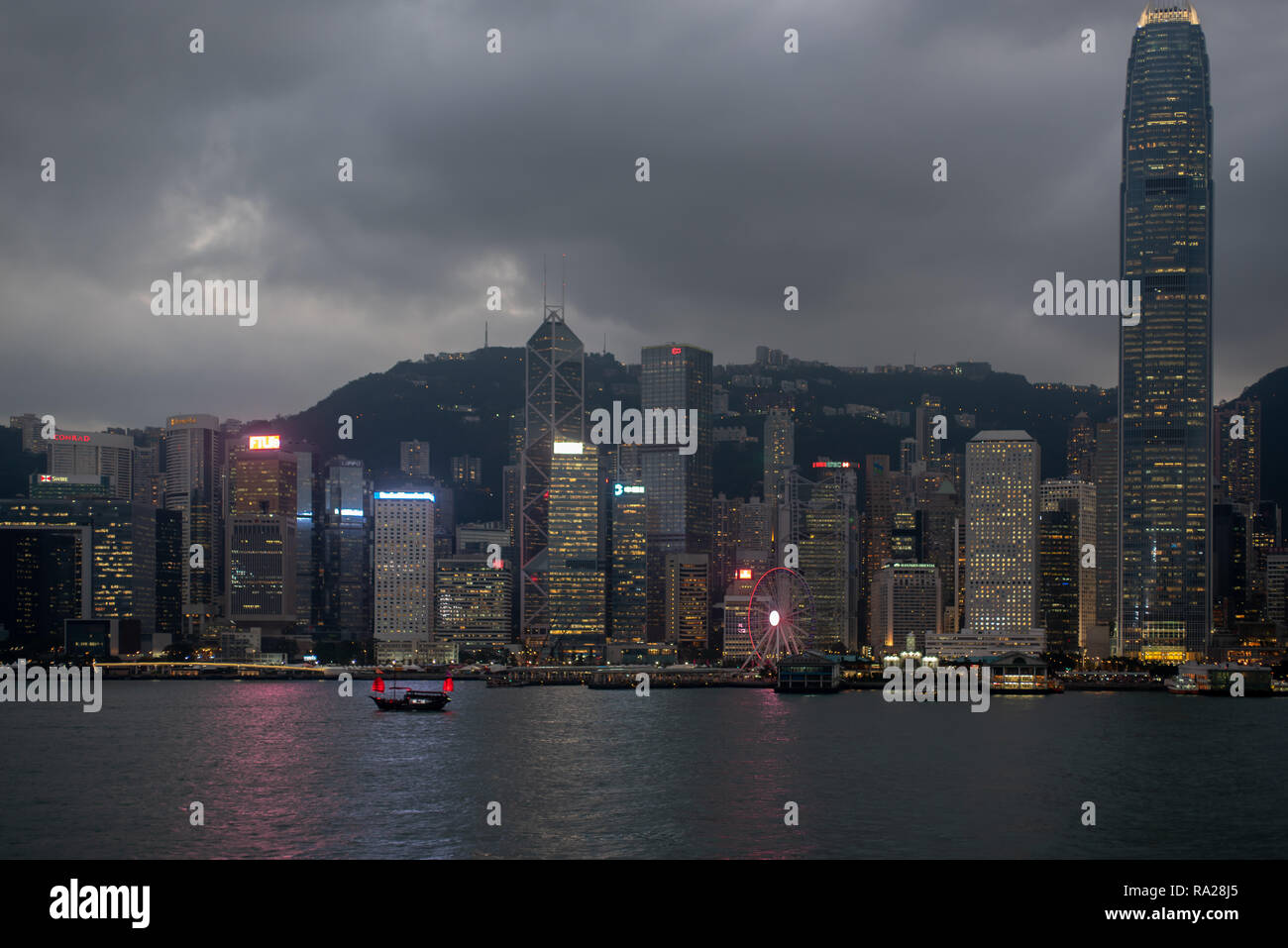 Die leuchtend rote Segel der Duk Ling touristische junk Akzente die Lichter der Wolkenkratzer, die Fringe Hafen von Hong Kong. Stockfoto