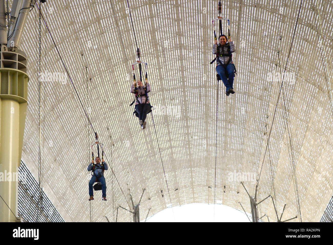 Drei Personen fliegen auf der SlotZilla Zipline unter dem tonnengewölbten Baldachin an der Fremont Street Experience im Stadtzentrum von Las Vegas, NV Stockfoto