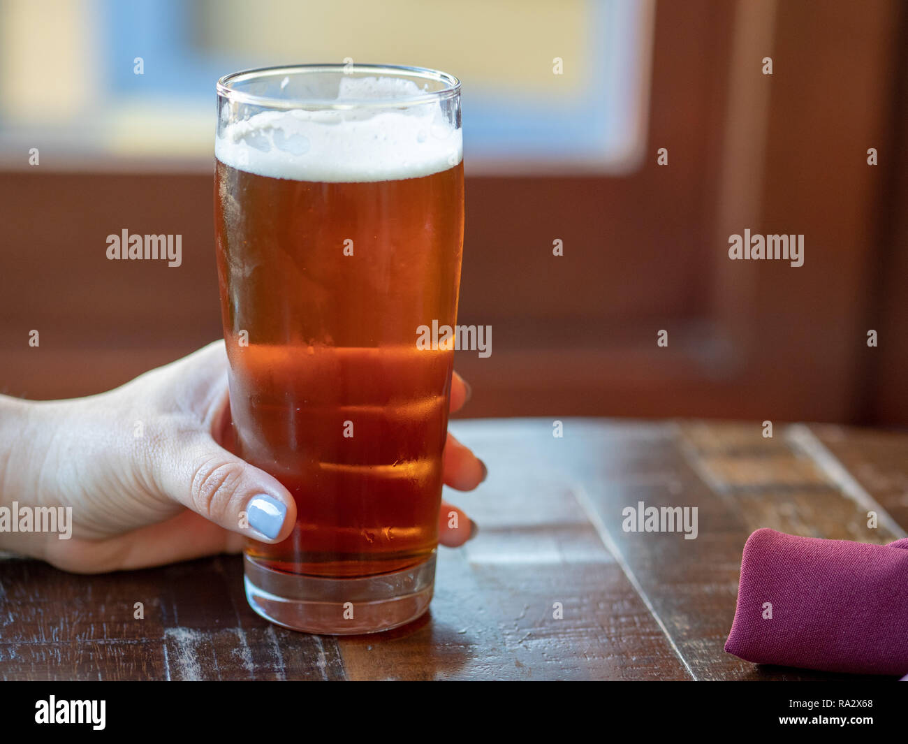 Frau mit rosa Fingernägeln holding Glas IPA Bier am Tisch im Restaurant Stockfoto