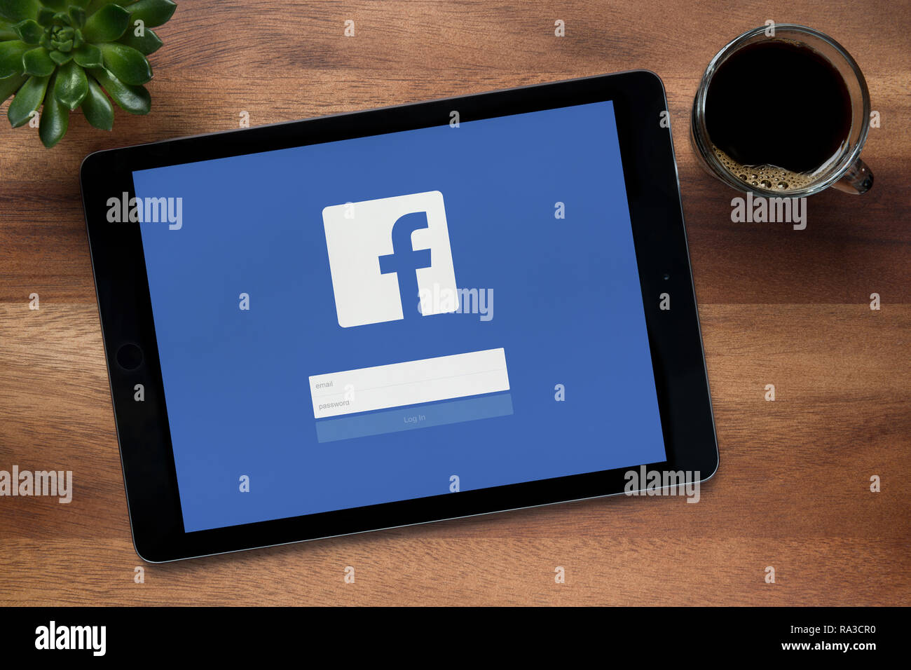 Facebook ist auf einem iPad Tablet gesehen, auf einer hölzernen Tisch zusammen mit einem Espresso und einem Haus Anlage (nur redaktionelle Nutzung). Stockfoto