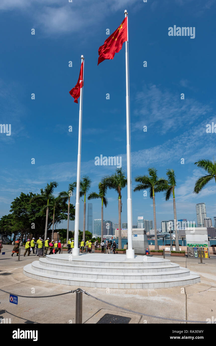 Die Hong Kong und Chinesischen Fahnen wehen über Golden Bauhinia Square mit, im Hintergrund, eine chinesische Reisegruppe tragen Hi-viz Jacken. Stockfoto