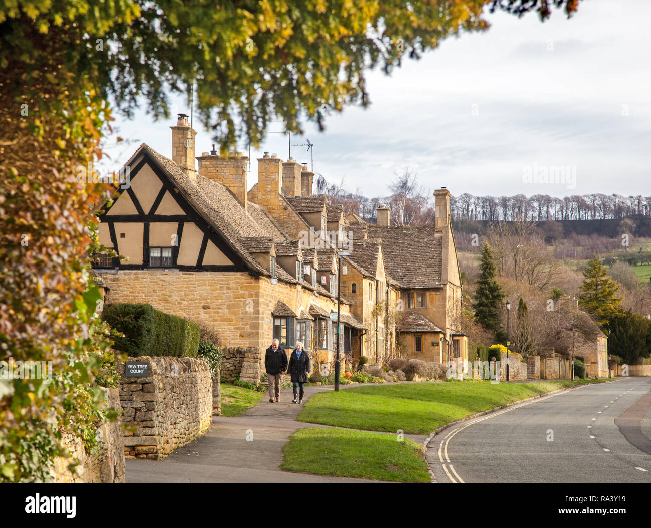 Mann und Frau ein Spaziergang durch die malerischen fundamentale Cotswold Village der Broadway mit seinen Cotswold stone Gebäude und Häuser Stockfoto