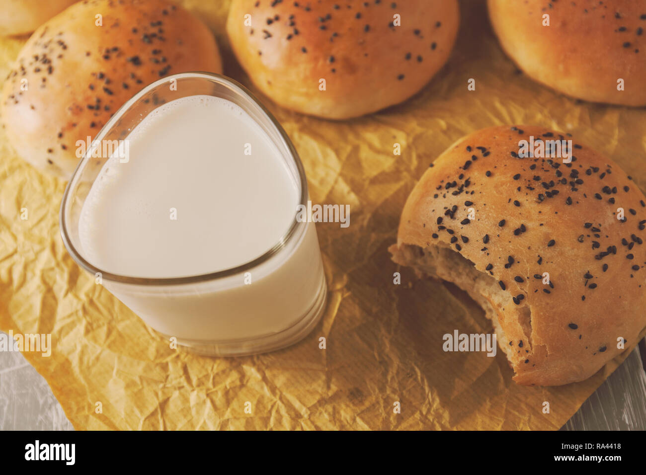 Frisch gebackene Burger Brötchen mit schwarzem Sesam auf einem backpapier. Frisch aus dem Ofen. Glas Milch Stockfoto