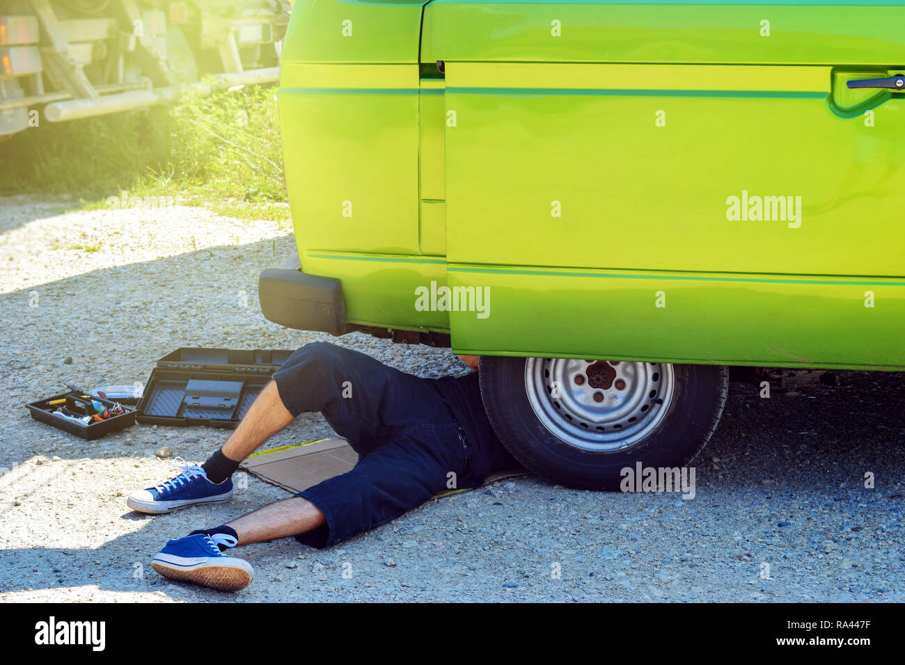 Junge männliche Hipster unter seinem alten Lügen-timer Camper versuchen, es neben der Straße zu reparieren Stockfoto