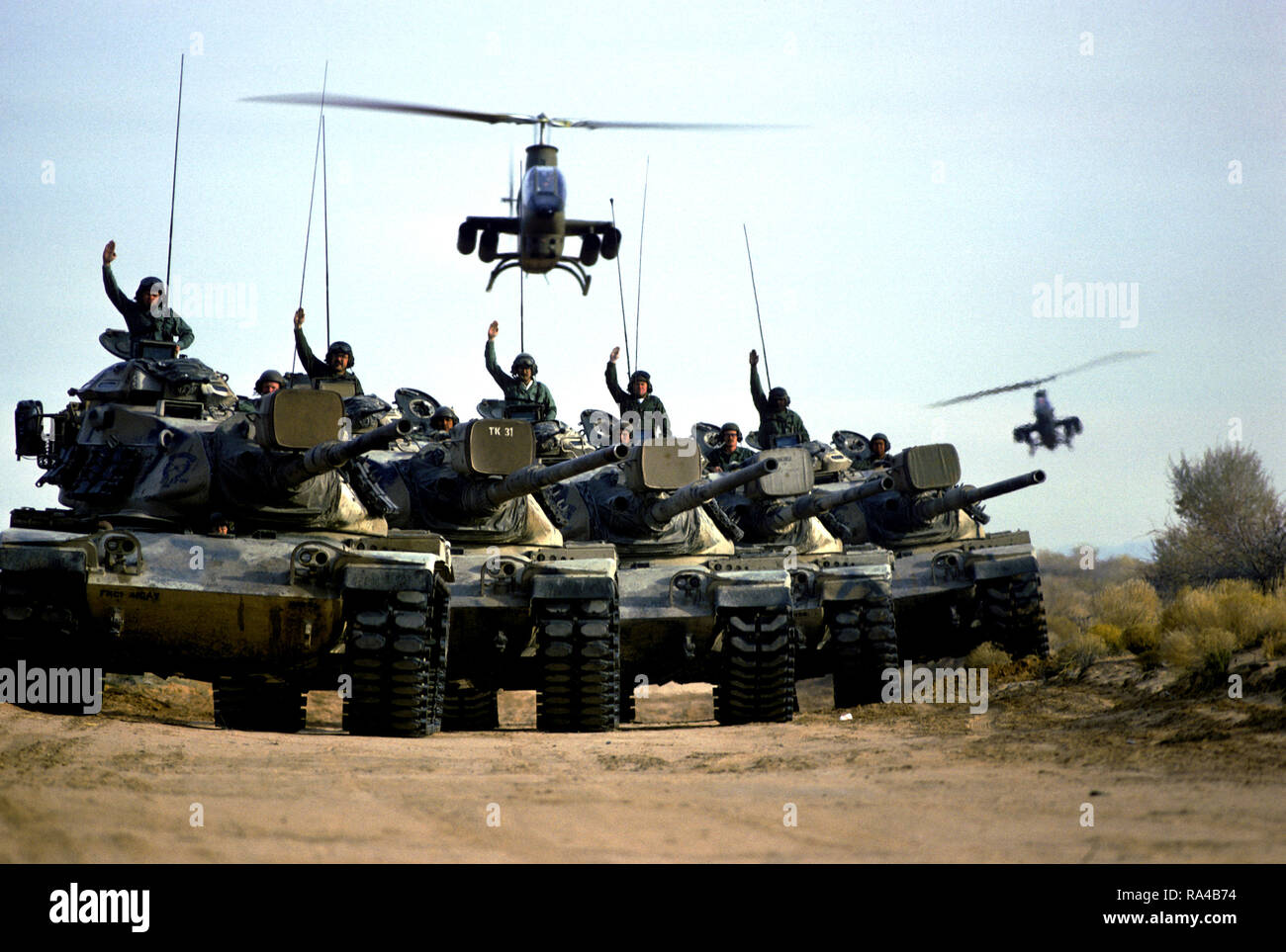 1974 - US-Army Soldaten geben Handzeichen von M 60 Kampfpanzer im Bereich Training. Zwei AH-1 Cobra Helikopter schweben Overhead. Stockfoto