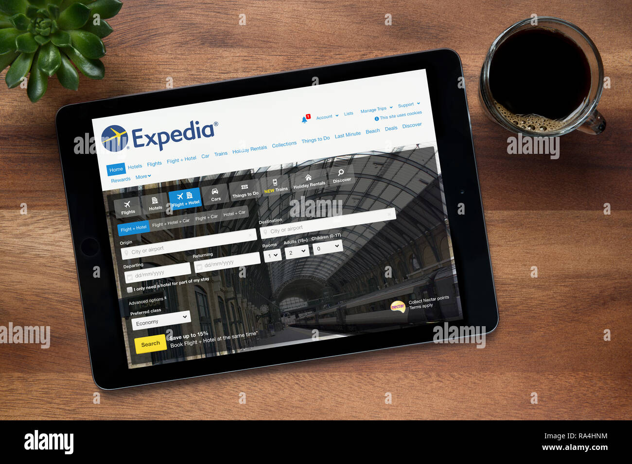 Die Website von Expedia ist auf einem iPad Tablet gesehen, auf einer hölzernen Tisch zusammen mit einem Espresso und einem Haus Anlage (nur redaktionelle Nutzung). Stockfoto