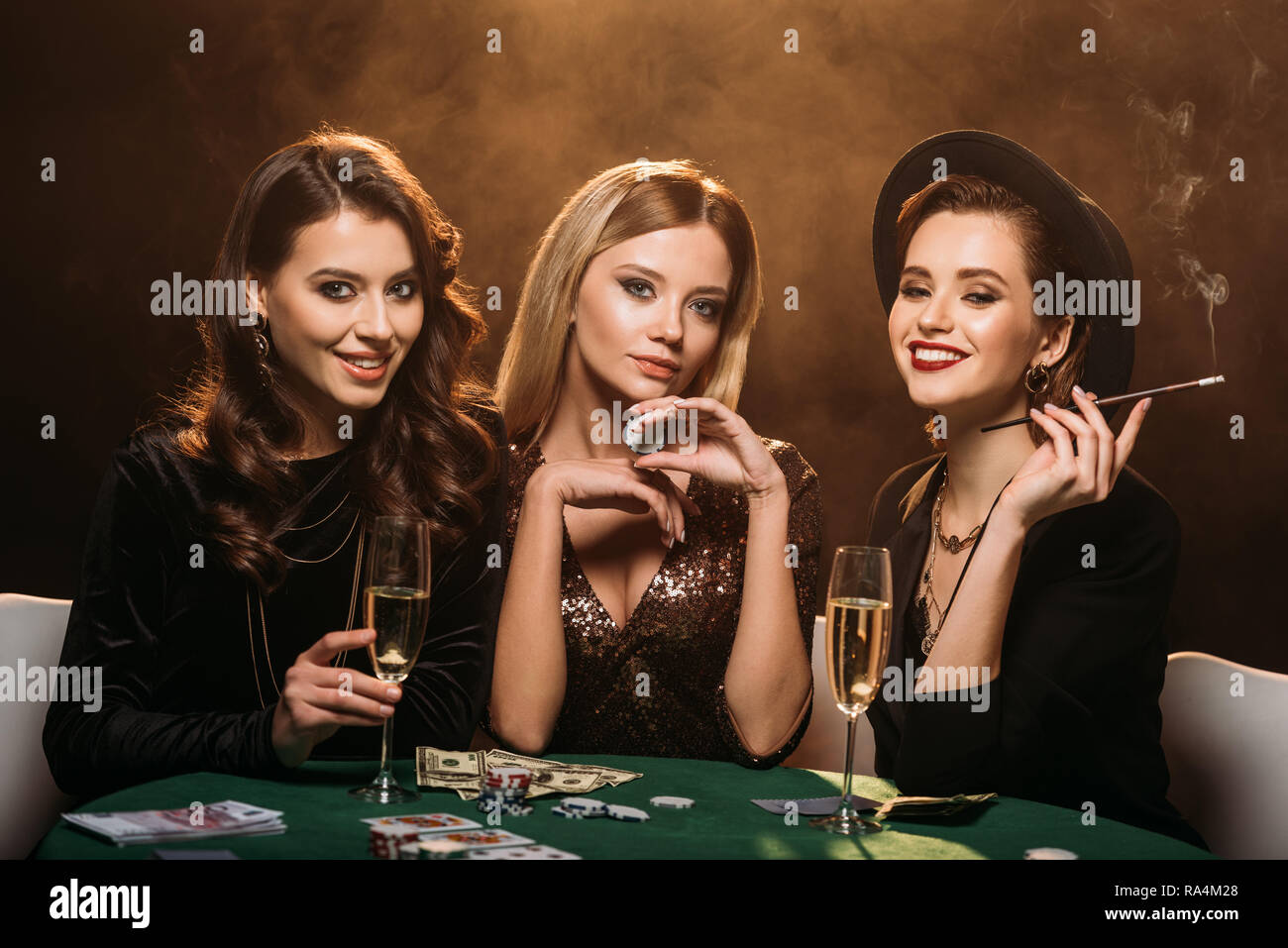 Sehr schöne Frauen mit einem Glas Champagner, Zigaretten und Poker Chips am Tisch sitzen in Casino Stockfoto