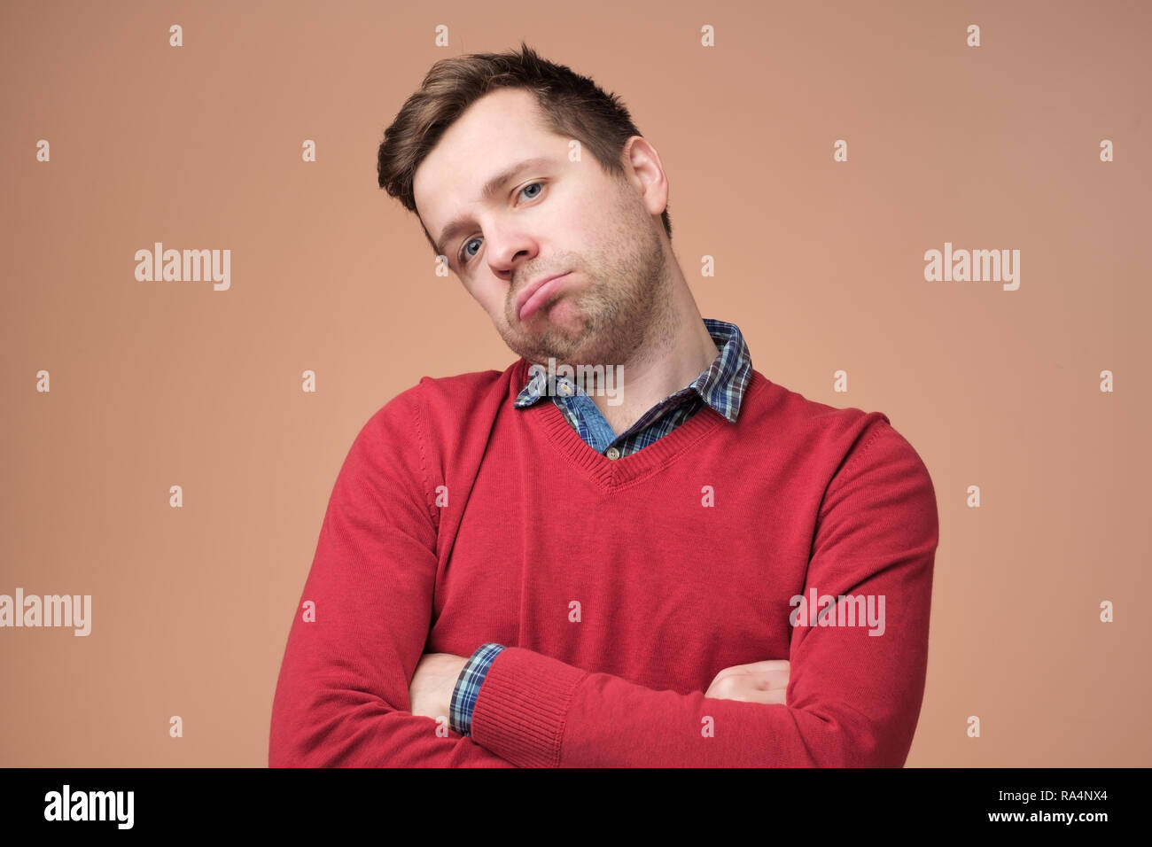 Traurige junge Mann im roten Pullover ist mit Arbeit erschöpft oder Müde des Hörens seiner Frau zu plaudern. Stockfoto