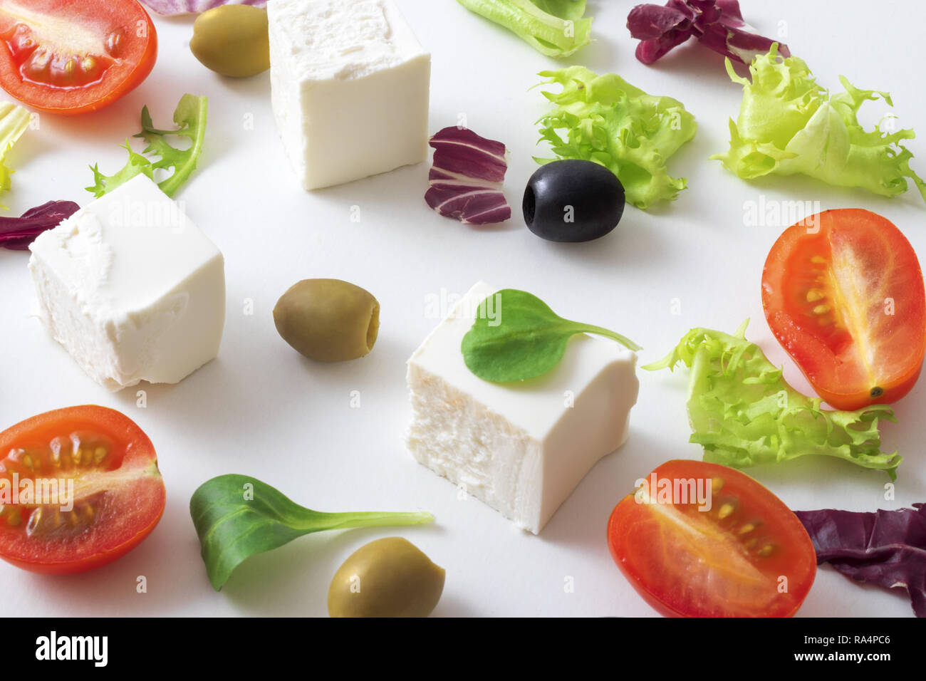 Griechischer Salat, weiß griechischer Käse, grüne und schwarze Oliven, Salatblätter, Hälften der Kirsche Tomate. Hintergrund weiss Variationen von salatblättern und Feta Stockfoto