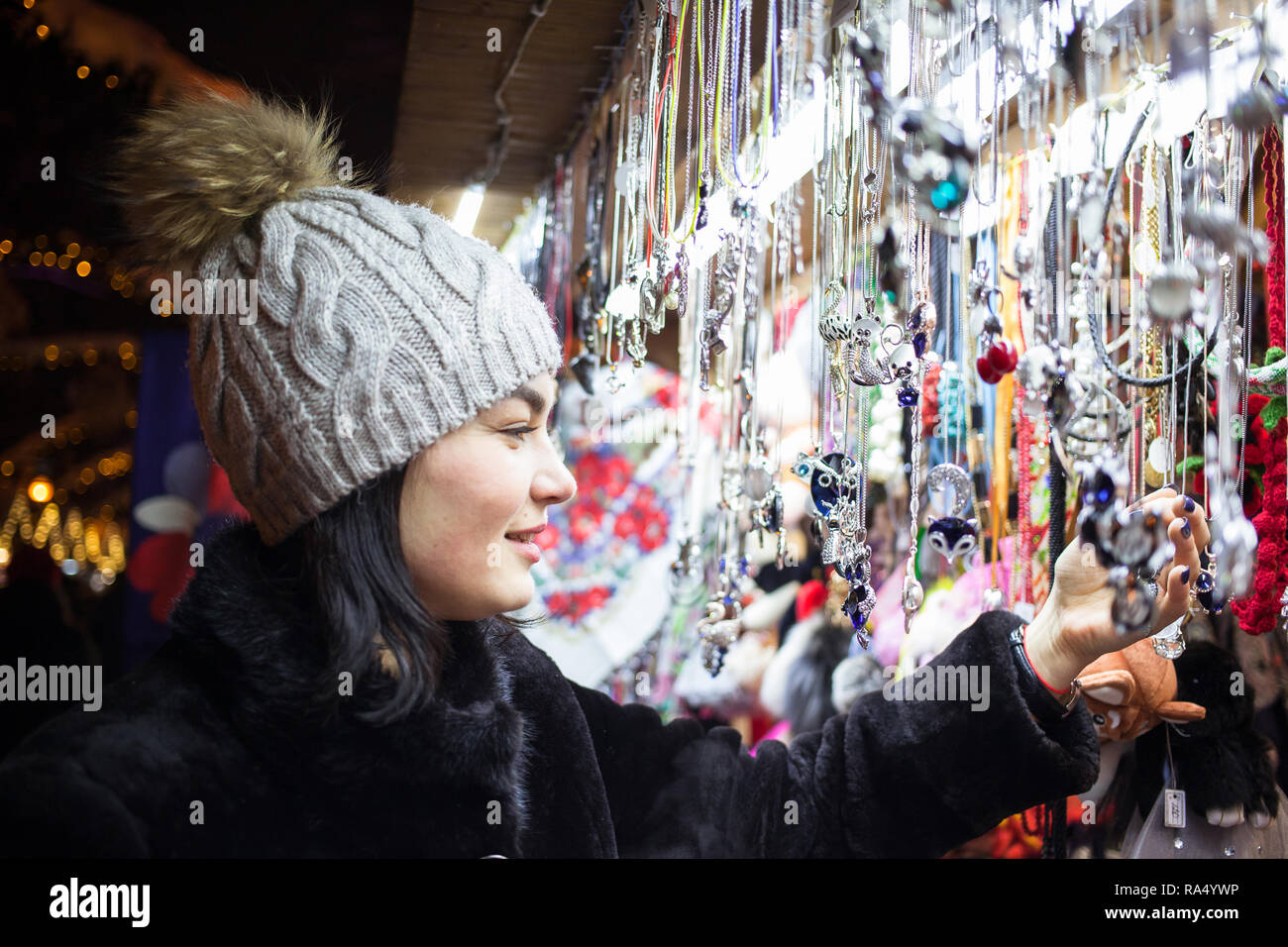 Glückliche junge Frau Wahl Weihnachten Dekoration am Markt. Modell tragen stilvolle Pelzmantel, gestrickte Mütze Hut. Outdoor Foto Stockfoto