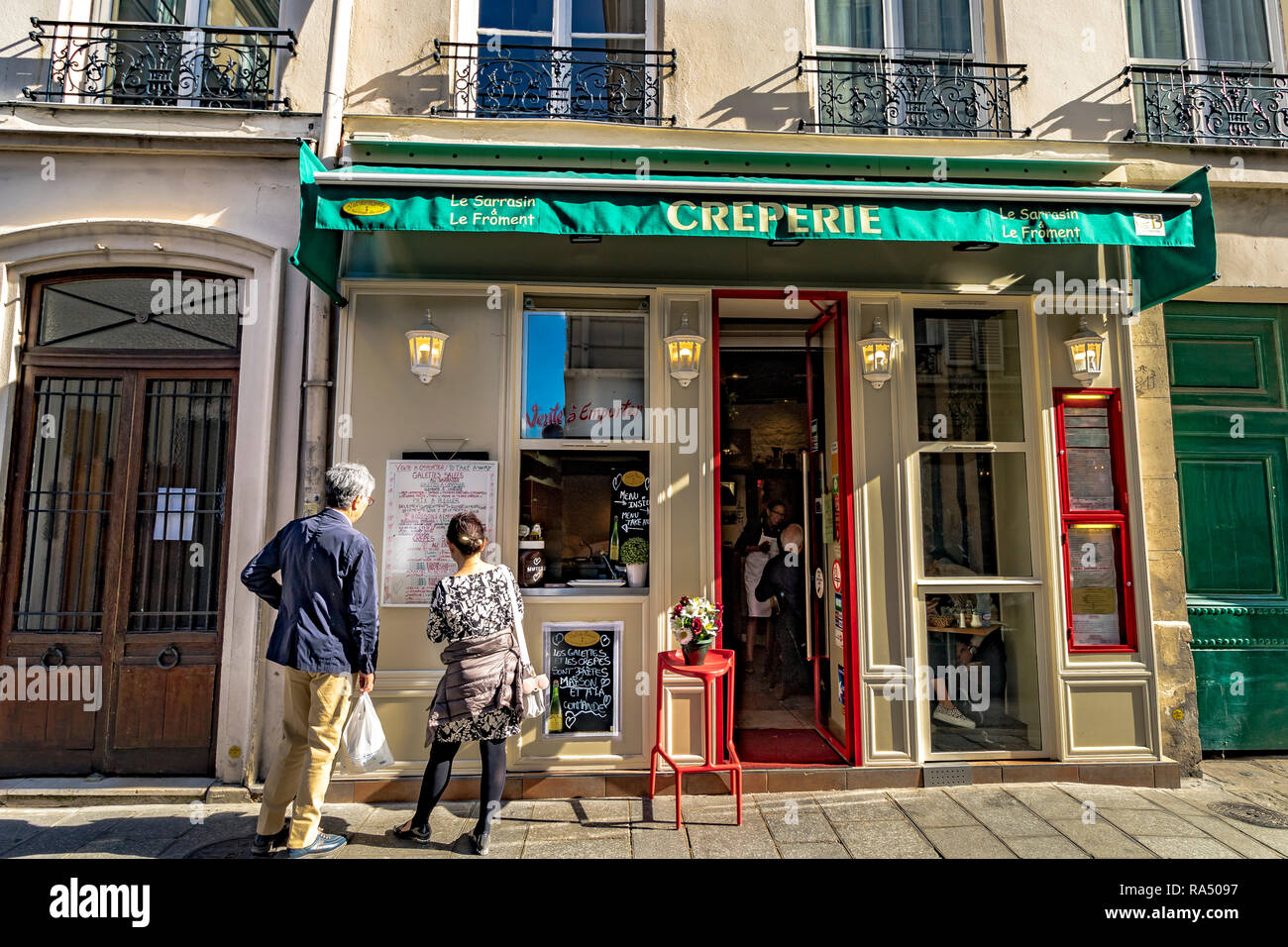 Ein Mann und eine Frau, die außerhalb Lesen der Speisekarte Sarrasin et le Froment Creperie in der rue Saint-Louis en l'Île, Paris Stockfoto