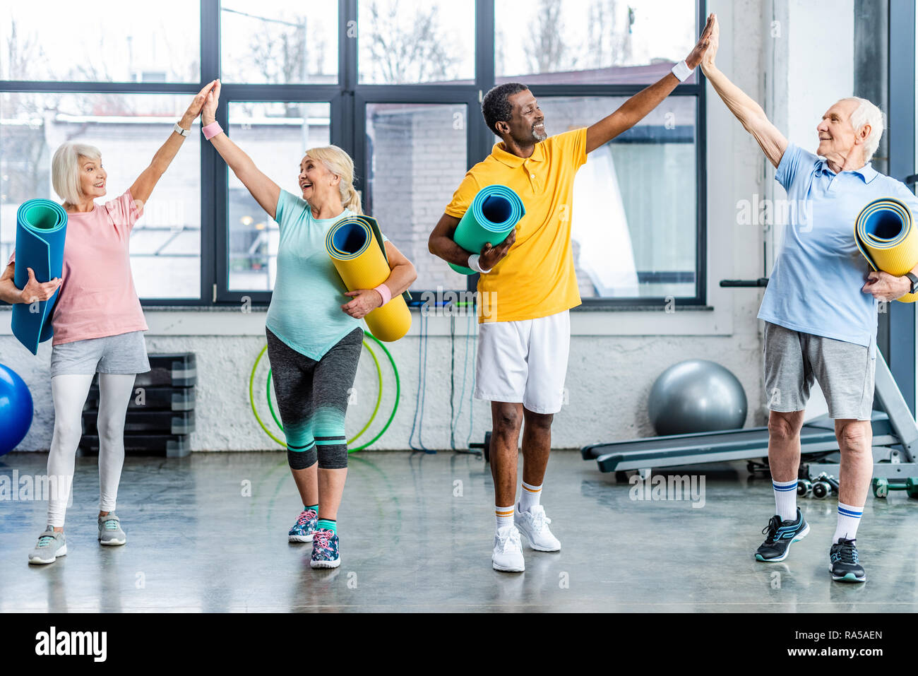 Lachend senior multiethnischen Athleten mit Fitness Matten unter High Fives miteinander im Fitnessstudio Stockfoto