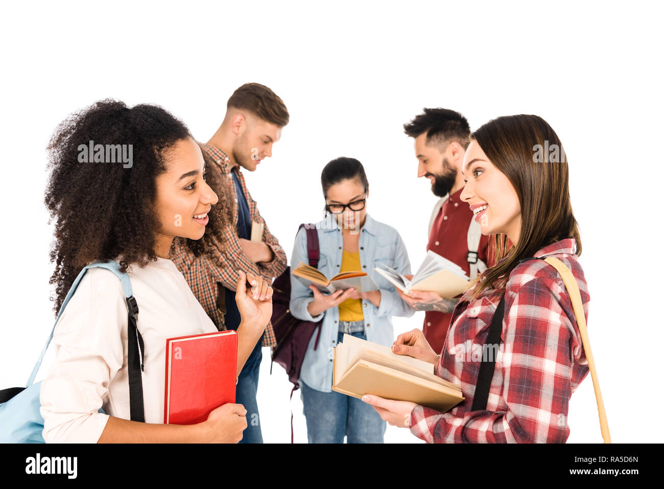 Attraktive multiethnischen Mädchen reden mit Büchern in der Hand in der Nähe der Gruppe junger Menschen isoliert auf weißem Stockfoto