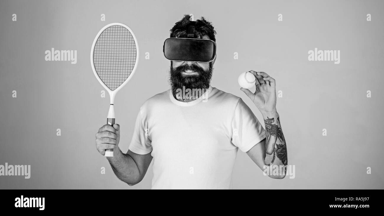 Kerl mit VR-Brille Tennis spielen mit Schläger und Ball. Mann mit Bart in VR -Brille Tennis spielen, grauen Hintergrund. Hipster auf lächelnde Gesicht  moderne Technologie für Sport Spiele. Virtueller Sport Konzept  Stockfotografie -