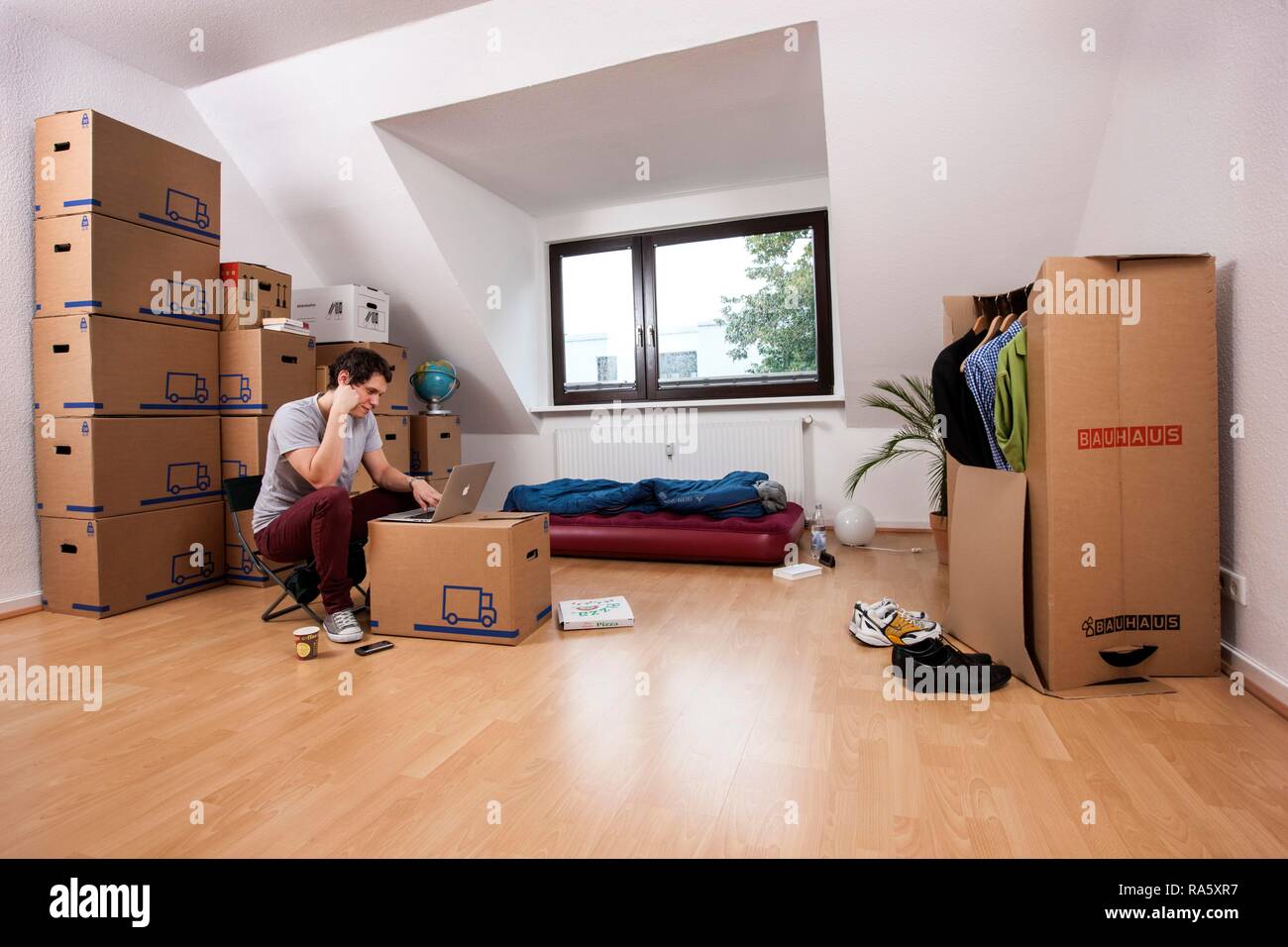 Junger Mann in einen leeren Raum in eine neue Wohnung sitzen, vorläufig mit  Schlafsack, Luftmatratze Stockfotografie - Alamy