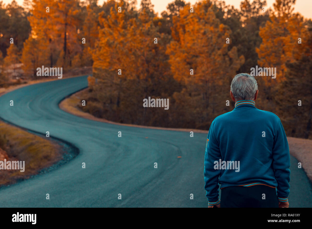 Aktiver älterer Mann steht alleine auf einsamen Straße zwischen Bergen. Ältere Mann zu Fuß zurück auf einsamen Highway Stockfoto