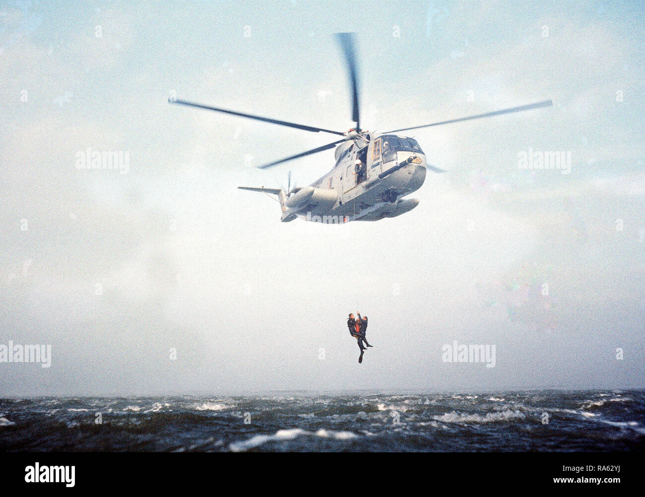 1977 - ein Meer-blick auf eine HH-3 Jolly Green Giant Hubschrauber mit einem Recovery hoist zwei pararescuemen aus dem Wasser vor der Küste von Kalifornien zu heben. Die Männer, von der die 129 für Luft- und Raumfahrt Rescue & Recovery Gruppe der Air National Guard, beteiligen sich an einer Praxis Rescue Mission. Stockfoto