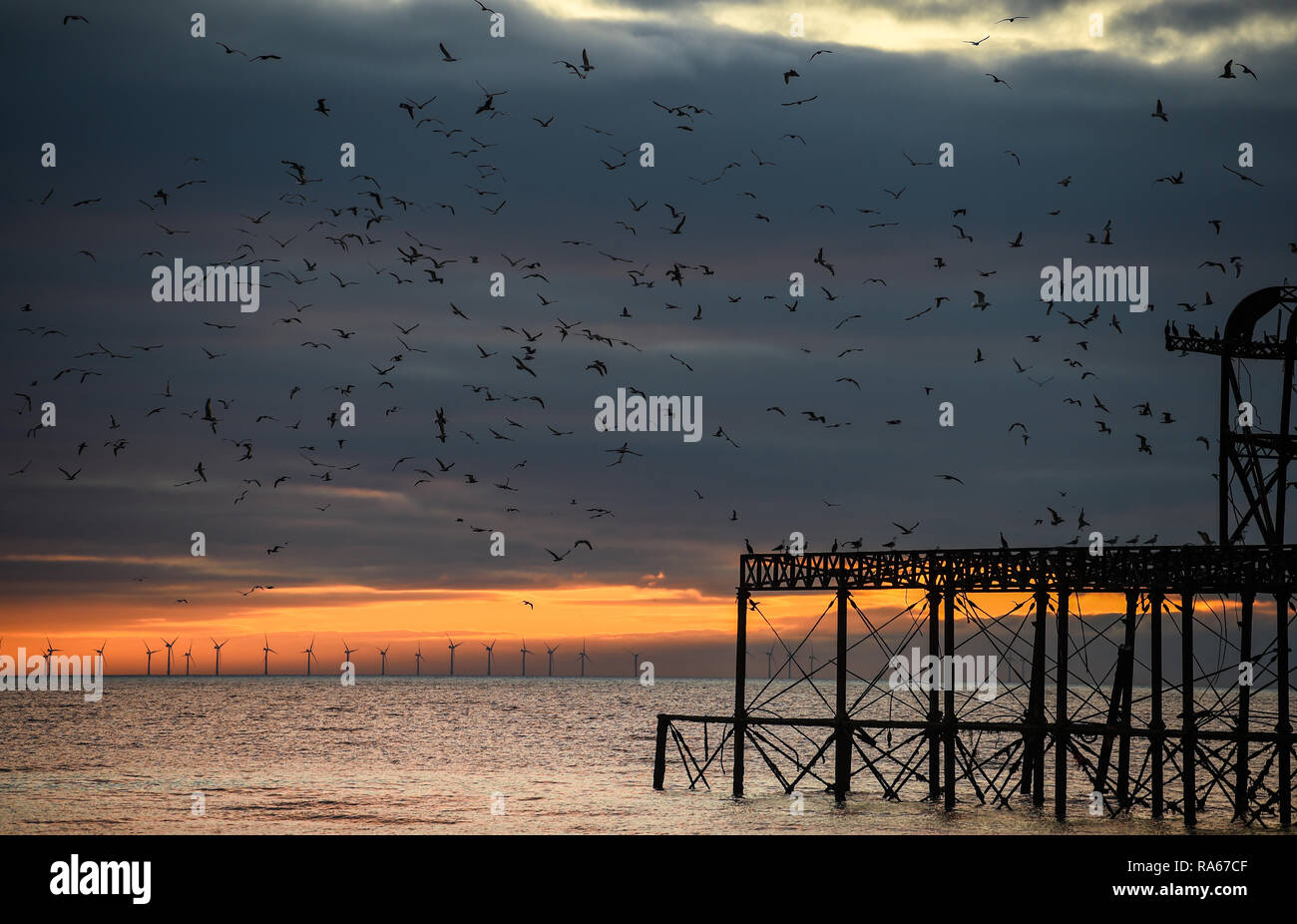 Brighton UK 1. Januar 2019 - die Sonne geht hinter der West Pier mit den Rapunzeln Windpark in der Ferne am Ende des schönen Nachmittag an der Südküste von Großbritannien: Simon Dack/Alamy leben Nachrichten Stockfoto