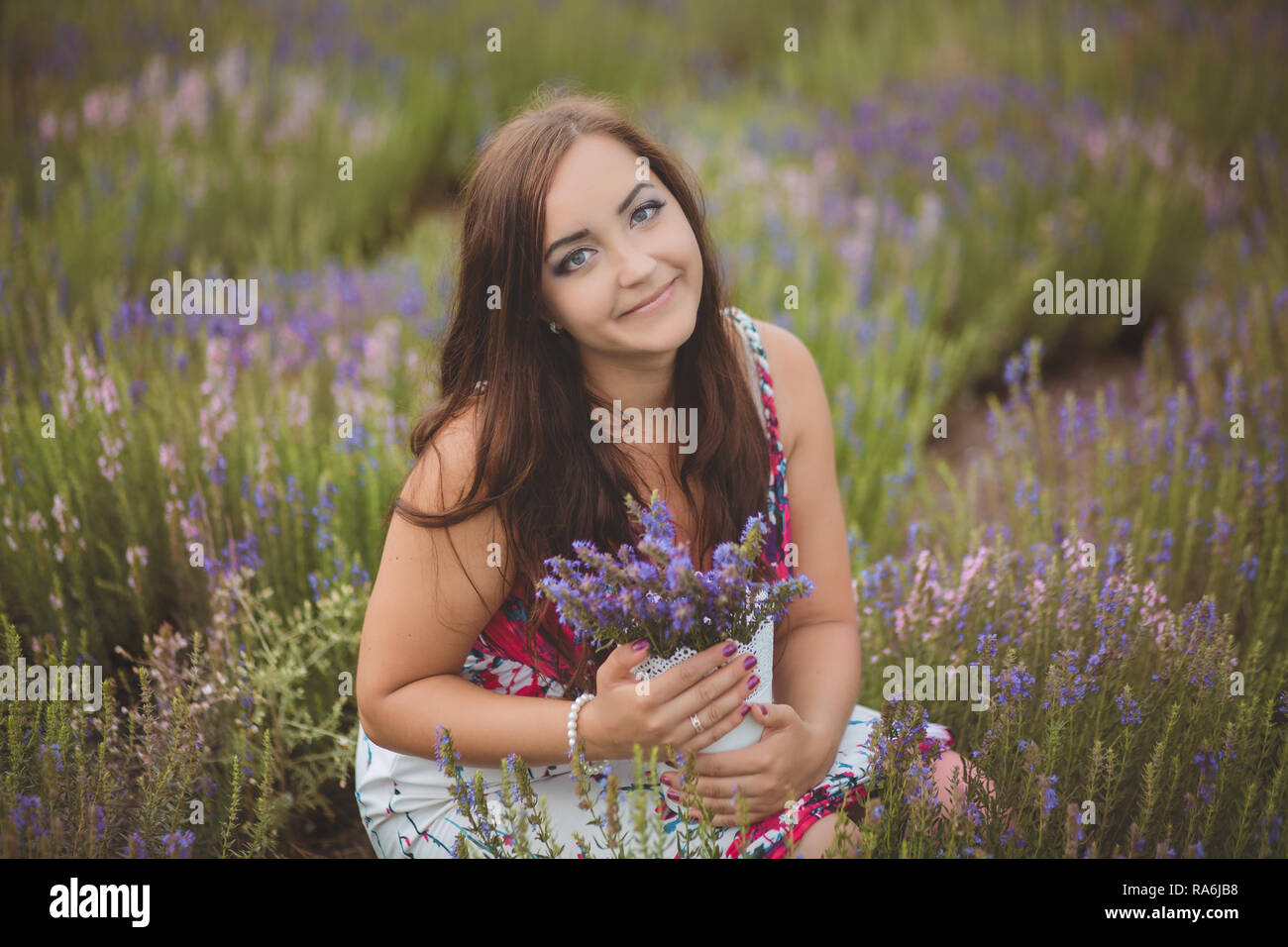 Schöne Brünette buxom nubile Dame Frau mit tiefen blauen Augen auf dem Gebiet der Feder Lavendel posing tragen nette gemütliche weiße Hand, Kleid und gedrückt halten. Stockfoto