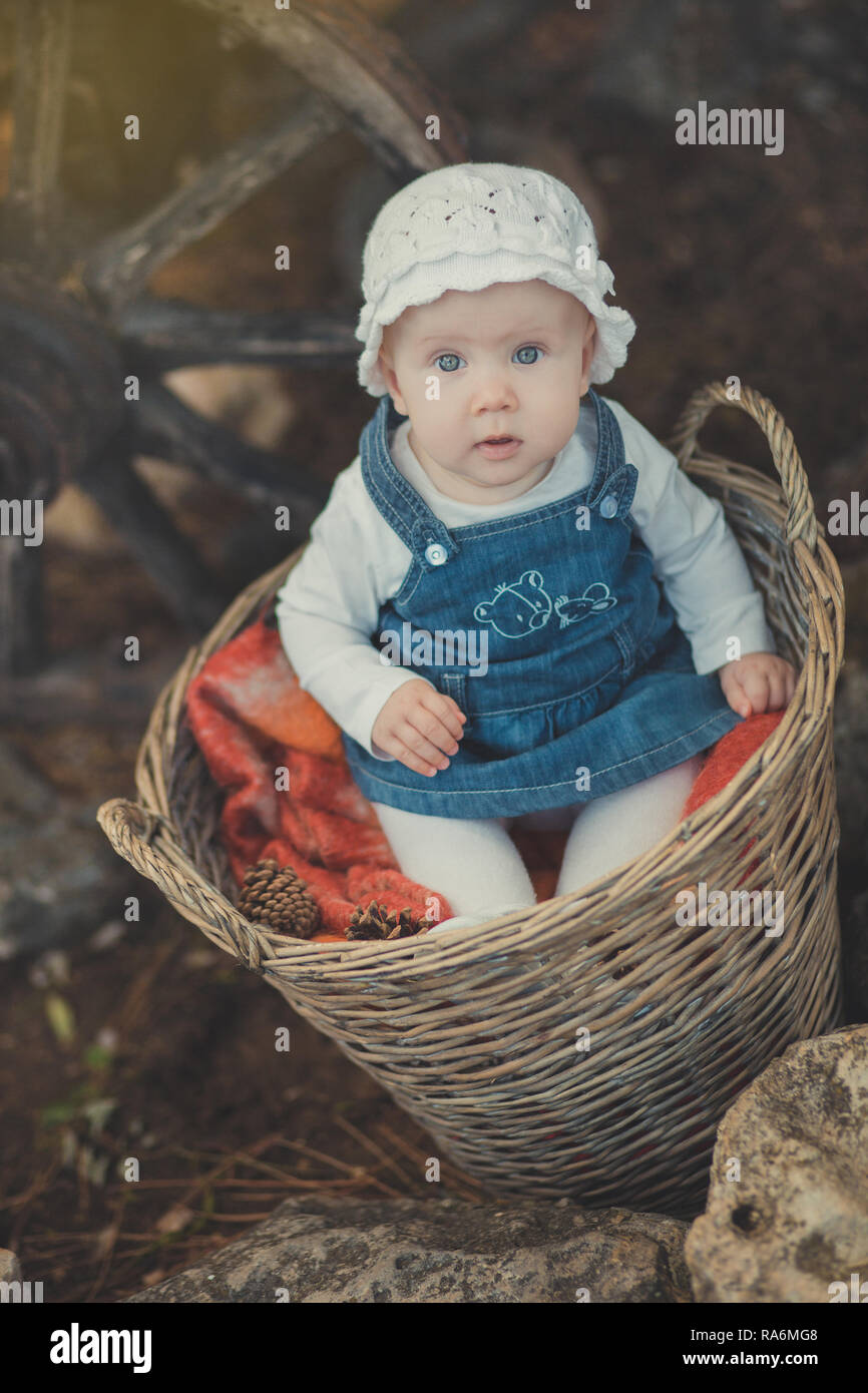 Baby Mädchen mit Ozean tief blauen Augen und pinky Wange tragen weiße Hemd  und Jeans Kleid und Handarbeit Handwerk tiny Hut sitzt in Korb in der Nähe  von woodwn Stockfotografie - Alamy