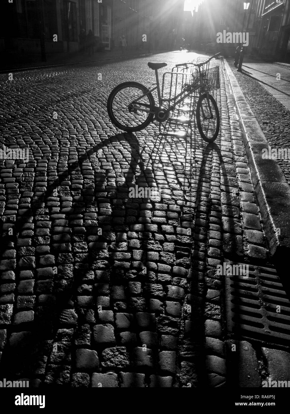 Mit dem Fahrrad auf einem Parkplatz fallen lange vertikale Schatten der alten Steinboden auf dem Sunset Stockfoto