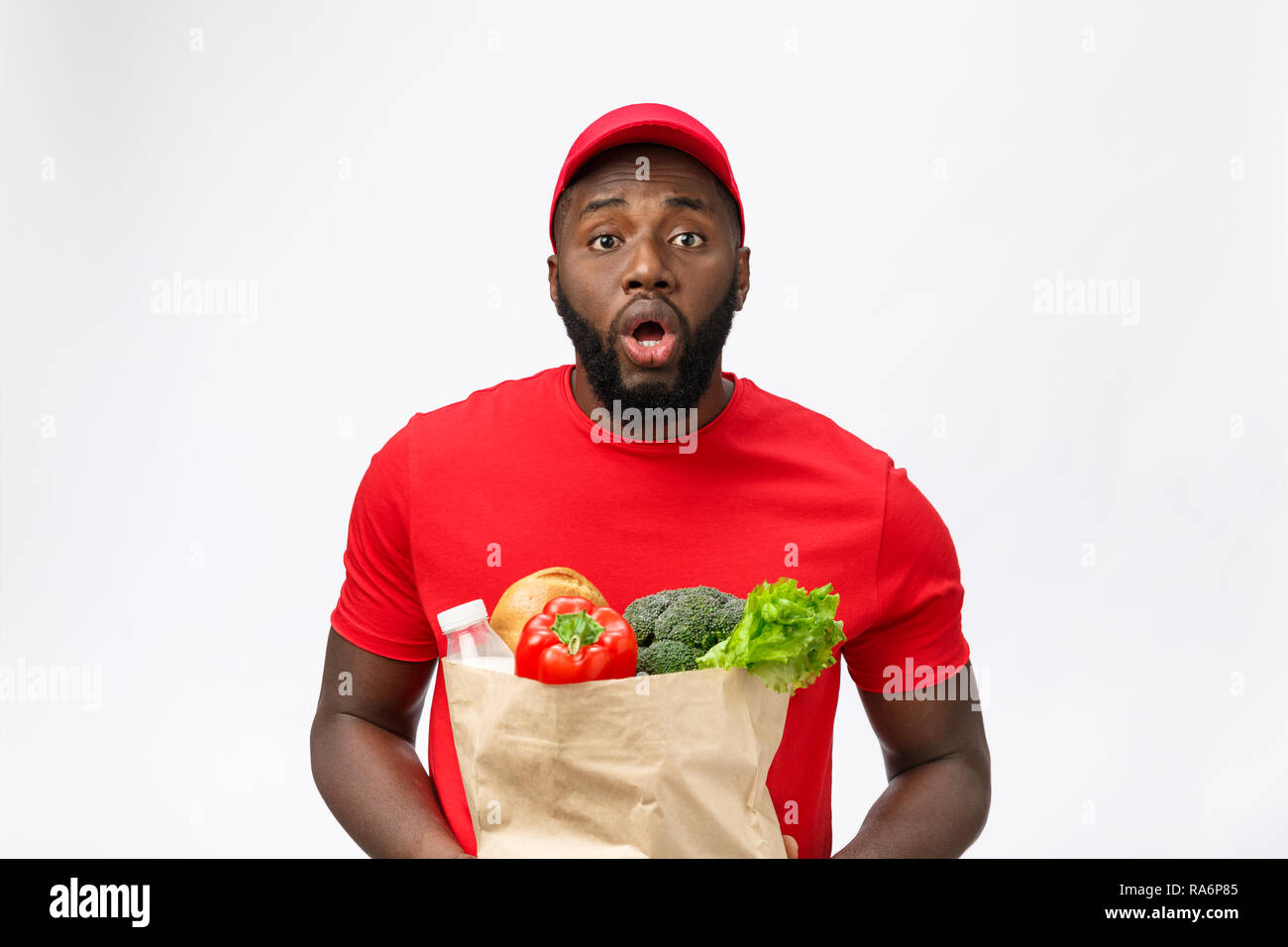 Junge afrikanische amerikanische Mann, Lebensmittelgeschäft Paket in den Händen mit schockierenden Gesicht. Über grauer Hintergrund isoliert. Stockfoto